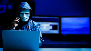 Anonymous hacker wearing mask using laptop to gain unauthorized access to Mazda internal system in cybersecurity breach scenario